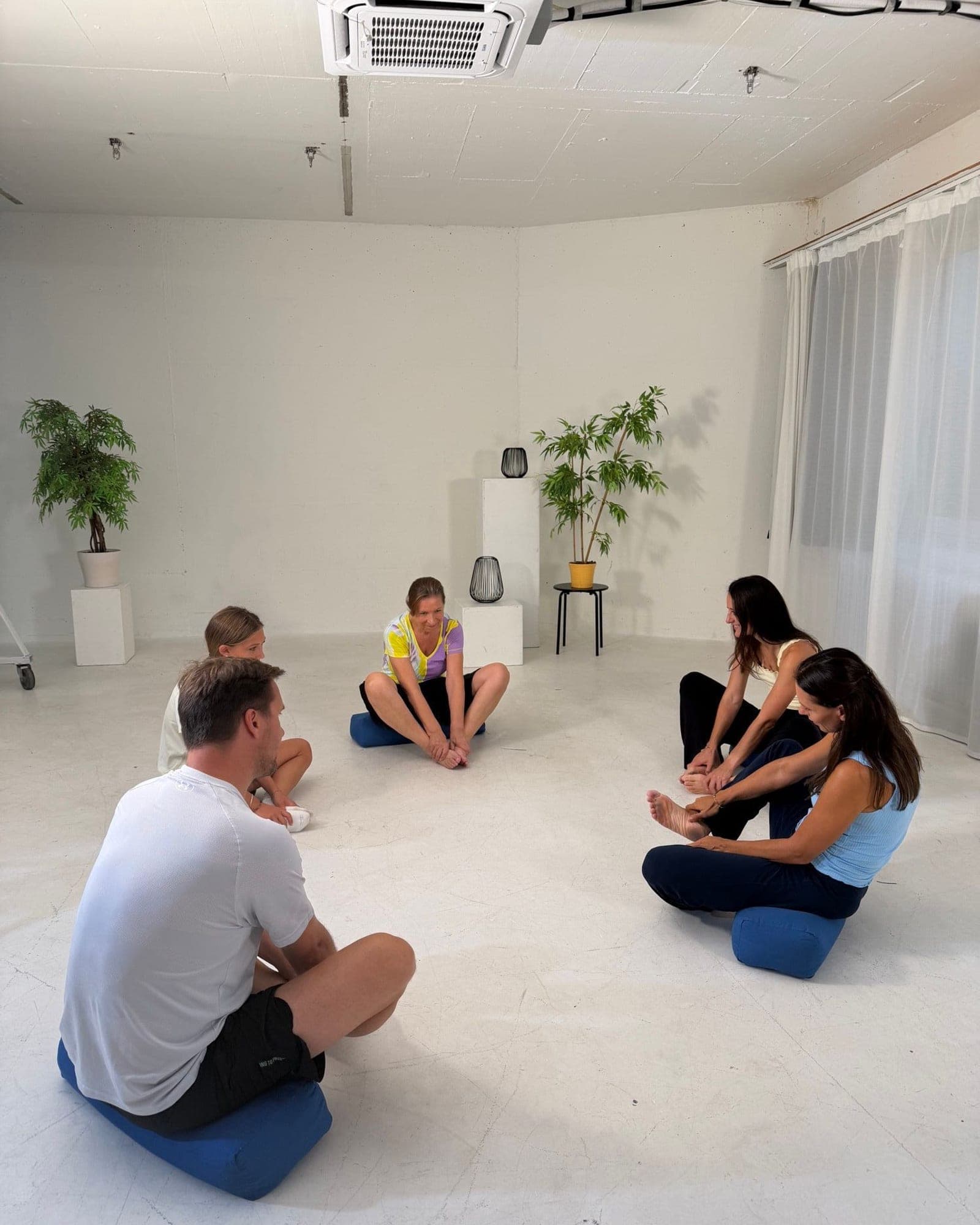 Workshop-Gruppe sitzt im Kreis auf Kissen und arbeitet an den Füßen
